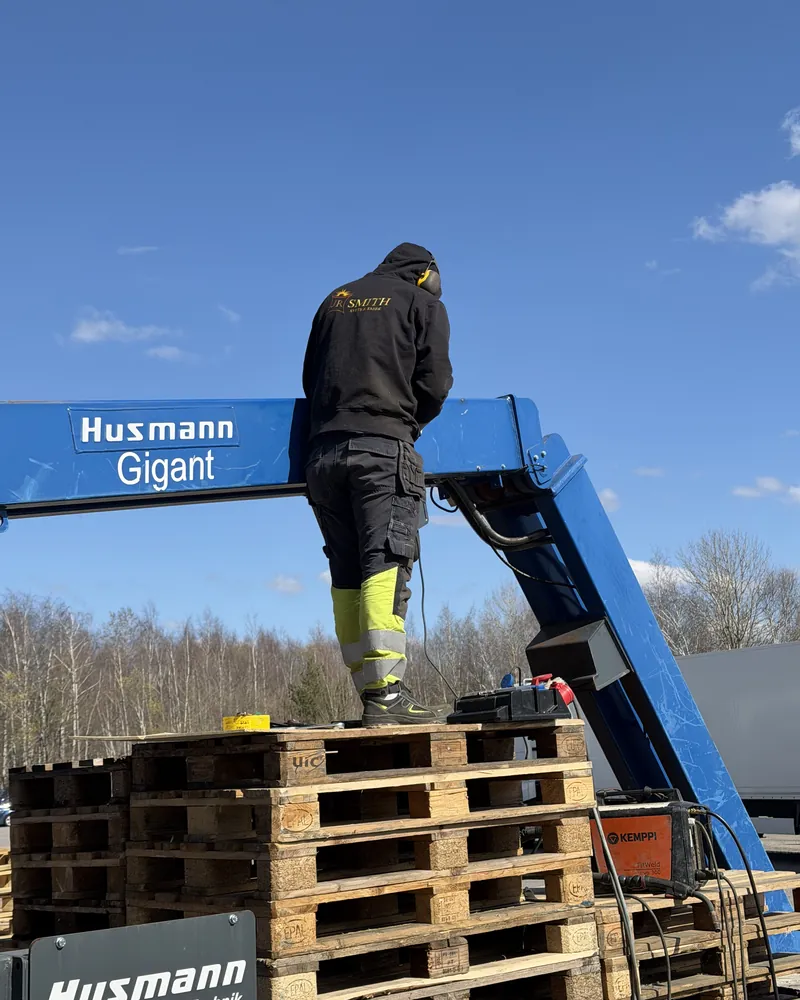 Svetsare står på lastpallar och svetsar på armen till en stor industrimaskin