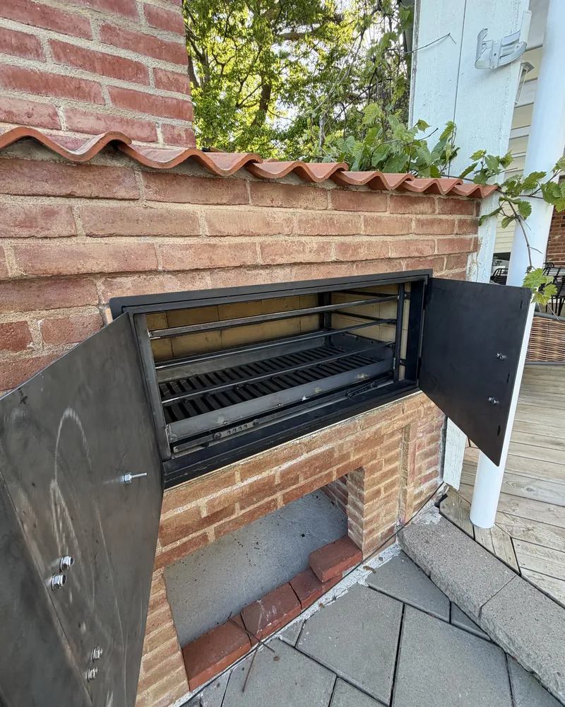 Öppna ståldörrar och justerbar grillinsats i stål i en murad utegrill